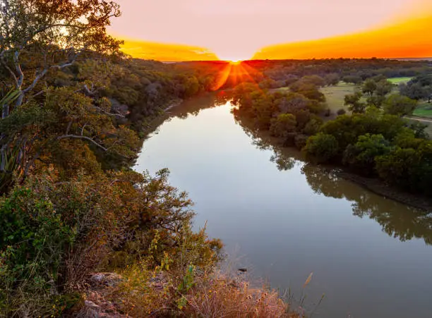 > High-angle view of a long, winding river cutting through a natural basin at sunset, illustrating the Colorado River journey where the water travels hundreds of miles over mineral-rich beds and limestone, heavily contributing to San Diego's hard municipal water supply.