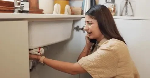 A stressed homeowner on a phone call checking a clogged kitchen sink drain, illustrating situations that require drain cleaning or hydro jetting and how much does a plumber cost in San Diego.