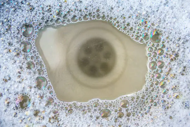 Close-up of soapy bubbles and dirty water pooling around a bathroom drain, illustrating why a tub or shower drain keep clogging.