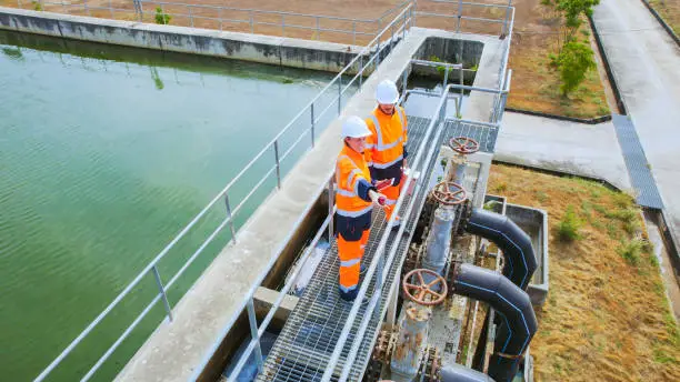 Two water utility technicians in hard hats and high-visibility vests inspect large intake valves next to an outdoor filtration basin, showcasing the process of moving imported water from regional supply lines to local San Diego treatment plants.