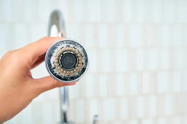 Close-up of a hand holding a pull-down kitchen faucet head covered in a thick ring of white crusty mineral scale, highlighting one of the most common visual signs of hard water in your home.