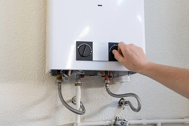 Person adjusting the control dial on a modern wall-mounted tankless water heater displaying narrow plumbing pipe connections.