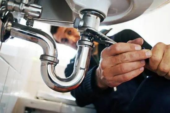 Plumber tightening a chrome sink trap P-trap with a wrench for San Diego plumbing maintenance guide.