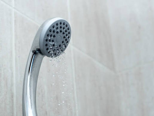 Chrome shower head spraying water with low water pressure.
