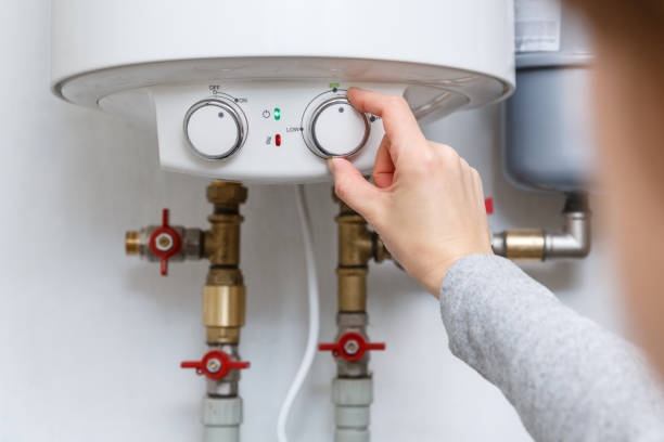 Close-up of a hand turning a white control dial on an indoor wall-mounted water heater unit.