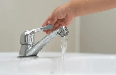 Hand adjusting a low-flow bathroom faucet running water for San Diego water conservation guide.