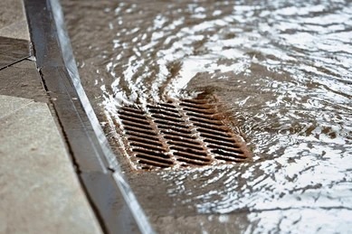 Rainwater and storm runoff rushing into an outdoor street drain sewer grate.