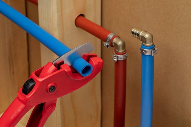 Plumber using red pipe cutter tool to cut blue PEX tubing during residential installation.