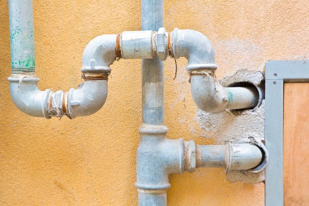 Exposed galvanized steel plumbing pipes and elbows mounted on exterior home wall.