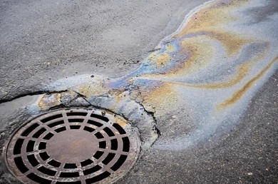 Oily, rainbow-colored water runoff flowing toward a round metal street storm drain