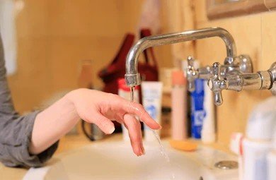 Weak stream of water trickling from faucet into bathroom sink.