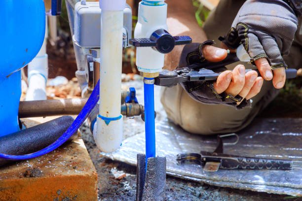 Plumber repairing blue water supply pipes damaged by long-term hard water mineral buildup.